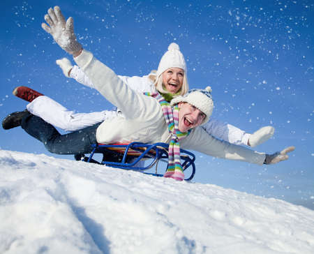 young couple having fun riding on a sled in the snow resortの写真素材