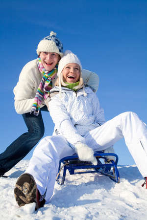 young couple having fun riding on a sled on a winter resortの写真素材