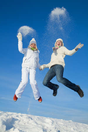 young couple having fun jumping on snowy hill in winterの写真素材