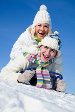 young couple having fun riding on a sled on a snowy hillの写真素材