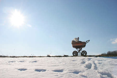 stroller with baby is on path of snow cover of the park under bright sunの写真素材