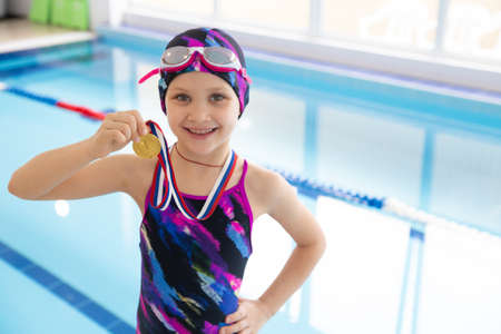 Portrait of little swimmer girl in swimming pool with medal for the first placeの写真素材