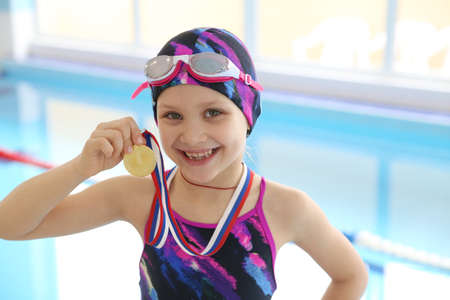 Portrait of little swimmer girl in swimming pool with medal for the first placeの写真素材