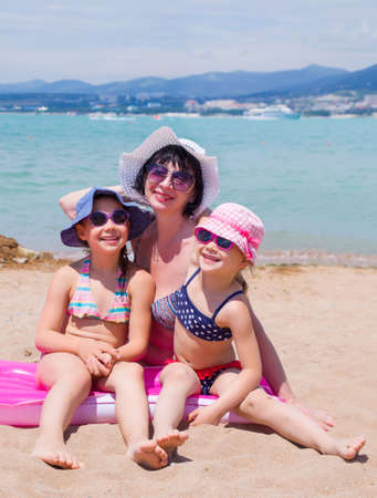 little girls with grandmother playing on a sandy beach and sunbathe in the sunの写真素材