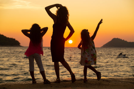 young woman with two children admiring the sunset on the sea coast. silhouette.の写真素材