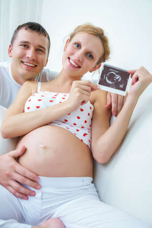 Young smiling couple holding and looking at an ultrasound scan of their expecting baby at homeの写真素材