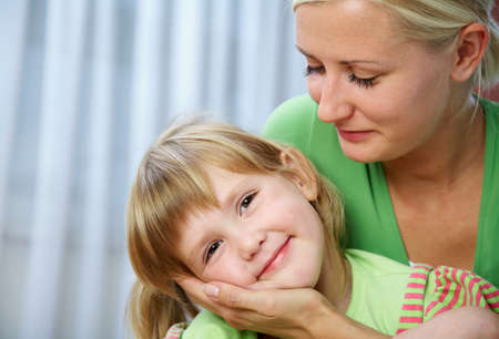 Young blonde mom tenderly hugs her little daughter at home.の写真素材