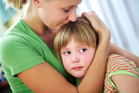 Young blonde mom tenderly hugs her little crying daughter at home.の写真素材