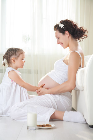 Little cute girl looking at her mother pregnant tummyの写真素材