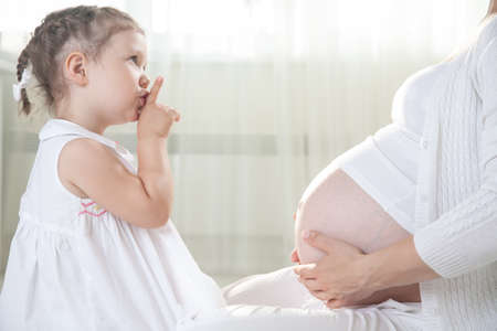 Little cute girl embracing her pregnant motherの写真素材