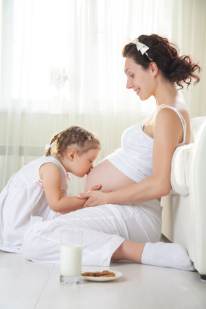 Little cute girl looking at her mother pregnant tummyの写真素材