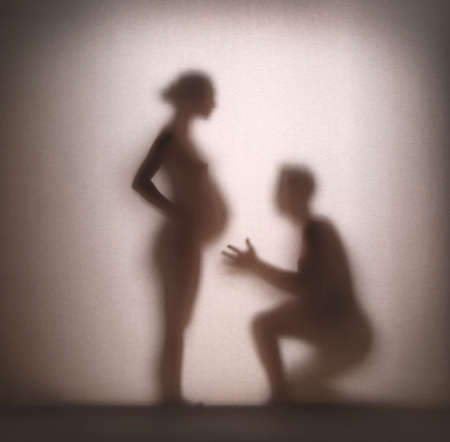 Beautiful silhouette of a young family expecting a baby blurred through the paper. A man and a woman rejoice at their first pregnancy.の写真素材