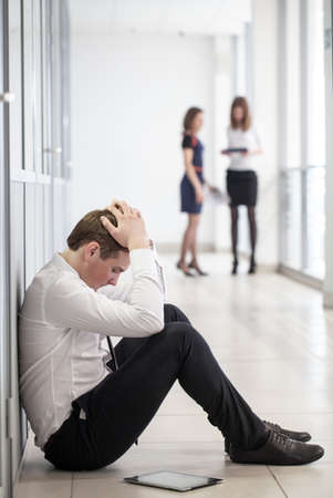 young business man sitting against in office wall in crisis momentの写真素材