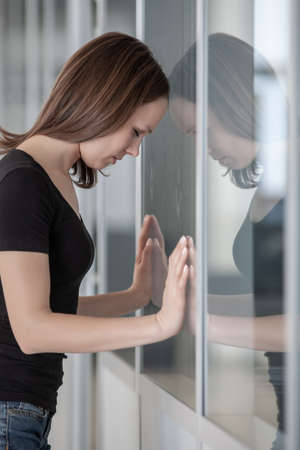 young woman woman leaned against glass wall in crisis momentの写真素材
