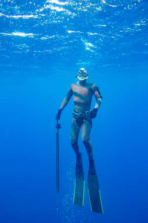 Underwater hunter with gun dives into the depths of the seaの写真素材