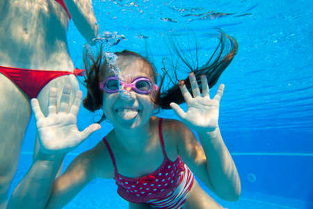Cheerful little girl swiming under water in pool.の写真素材