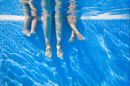 4 pairs of feet under water in a swimming poolの写真素材