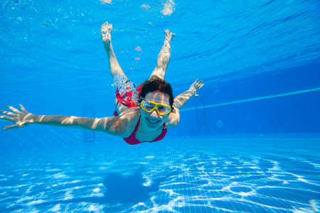 young woman dives into the swimming pool with bubbles. Underwater photoの写真素材