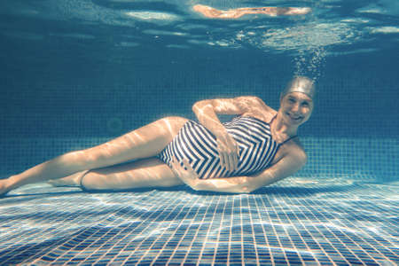 pregnant woman diving in a pool of blue water. Underwater photo.の写真素材