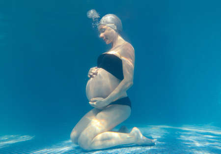 Beautiful pregnant woman dives in a pool with blue water. Underwater photography.の写真素材