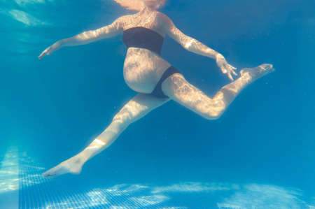 pregnant woman relaxes in a pool of blue water. Unrecognizable body. Underwater photo.の写真素材