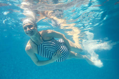Beautiful pregnant woman dives in a pool with blue water. Underwater photography.の写真素材