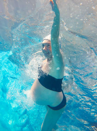 pregnant woman swimming in a pool of blue water. Underwater photo.の写真素材