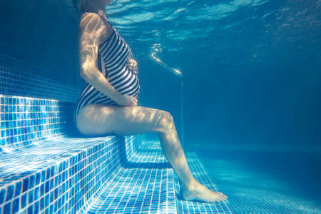 pregnant woman relaxes in a pool of blue water. Unrecognizable body. Underwater photo.の写真素材