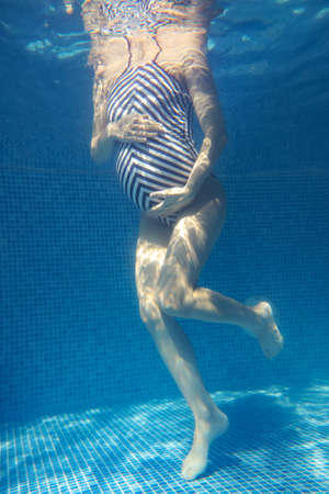 pregnant woman relaxes in a pool of blue water. Unrecognizable body. Underwater photo.の写真素材