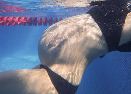 pregnant woman relaxes in a pool of blue water. Unrecognizable body.