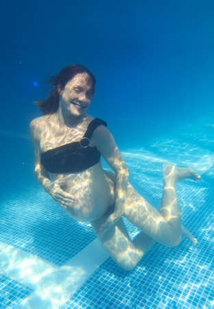Beautiful pregnant woman dives in a pool with blue water. Underwater photography.の写真素材
