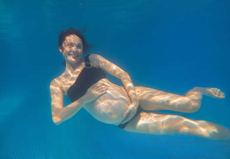 Beautiful pregnant woman dives in a pool with blue water. Underwater photography.の写真素材