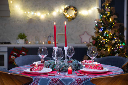 beautifully decorated Christmas table with candles and glasses near the Christmas tree