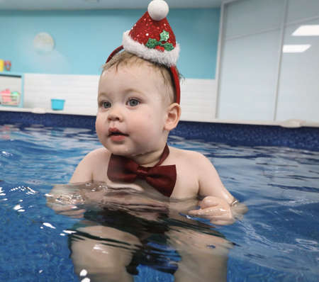baby boy in a Santa Claus hat dives in the pool with pleasure. Christmas picture.の写真素材
