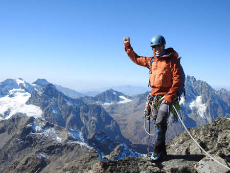 mountaineer with ice ax stands on the top of a mountain in the background of the landscape of snowy mountainsの写真素材