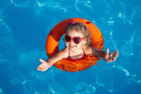 Funny little girl swims in a pool in an orange life preserverの写真素材