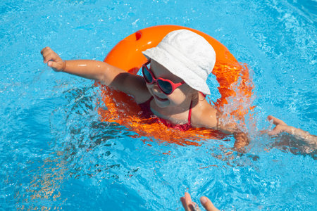 Funny little girl swims in a pool in an orange life preserverの写真素材