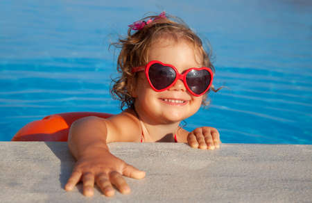 Funny little girl swims in a pool in an orange life preserverの写真素材