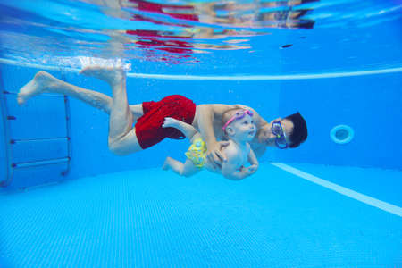 underwater photo of young dad with little boy in swimming pool