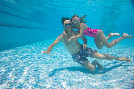 underwater photo of young dad with little girl in swimming poolの写真素材