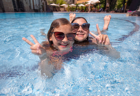 Two teenager girs having fun in swimming pool on resortの写真素材