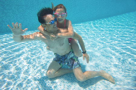 underwater photo of young dad with little girl in swimming poolの写真素材
