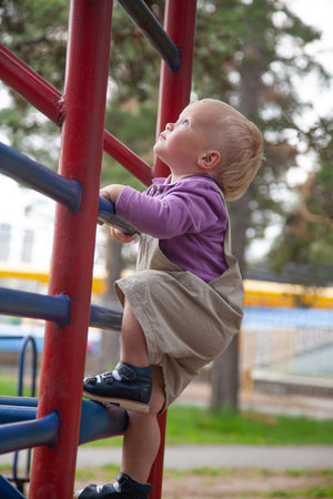 little boy climbs a ladder on a sports ground on the streetの写真素材