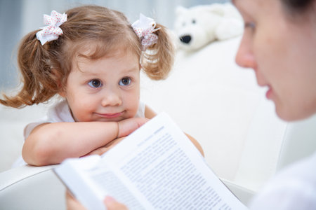 Mother reading book her cute little girl at homeの写真素材
