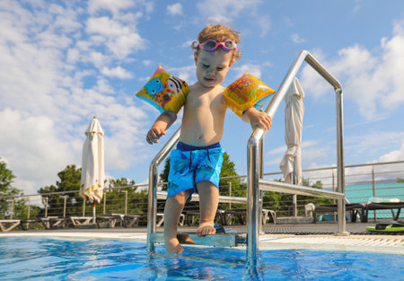 one-year-old boy is standing on the side of the pool with inflatable armlets.の写真素材