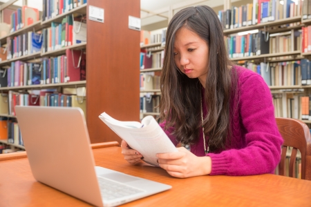 Woman with book and laptob studying in libraryの写真素材