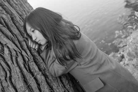 Portrait of young woman leaning against a tree next to a riverの写真素材