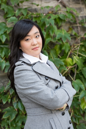 Young Asian woman standing next to leafs on a wall crossing her armsの写真素材