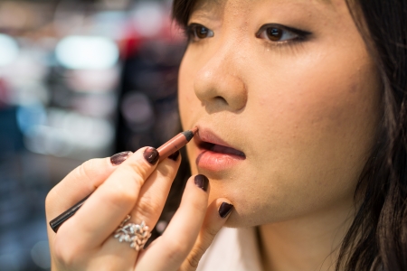 Young Asian woman applying lipstick and other cosmeticsの写真素材