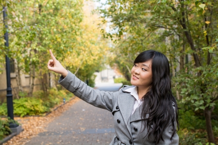 Portrait of young attractive girl pointing at something on the trees at the side of a roadの写真素材